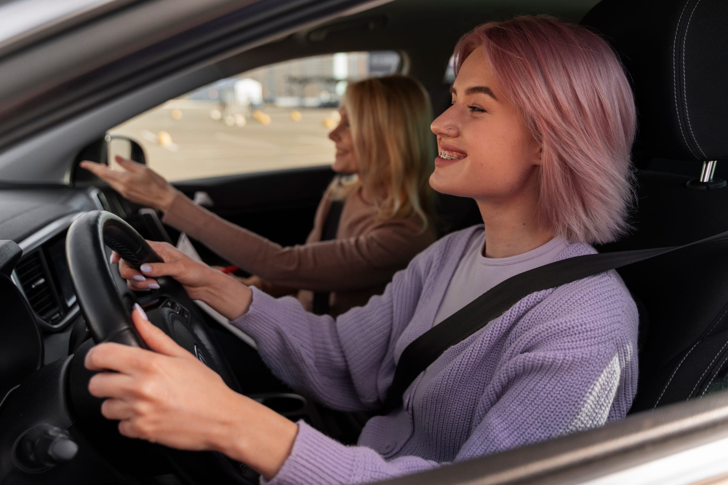 A smiling learner at the wheel with her instructor pointing the way ahead